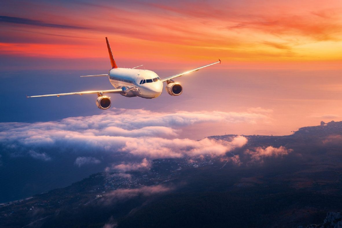 Passenger airplane. Landscape with big white airplane is flying in the sky over the clouds and sea at colorful sunset. Passenger aircraft is landing at dusk. Business trip. Commercial plane. Travel